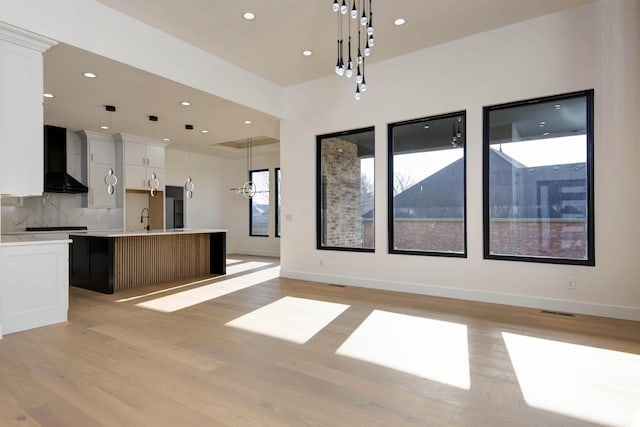 kitchen featuring an island with sink, decorative backsplash, light wood finished floors, and wall chimney exhaust hood