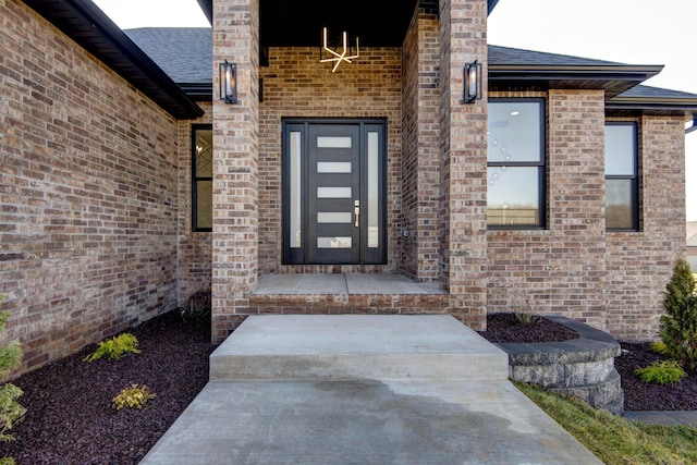 entrance to property featuring brick siding and a shingled roof