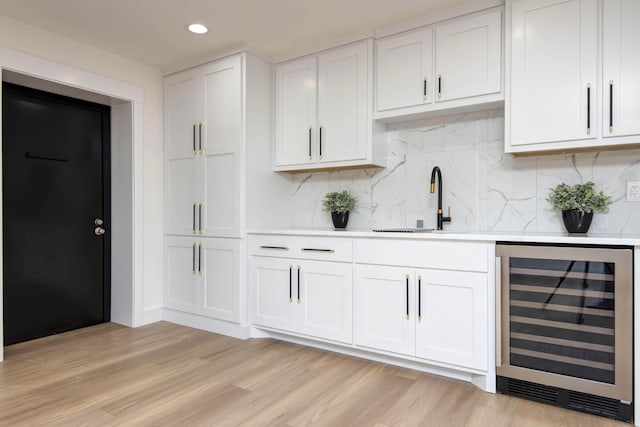 bar with light wood-type flooring, a sink, tasteful backsplash, wine cooler, and wet bar