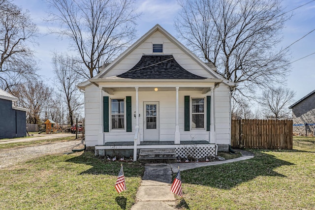 bungalow-style house featuring a front yard, fence, covered porch, and roof with shingles