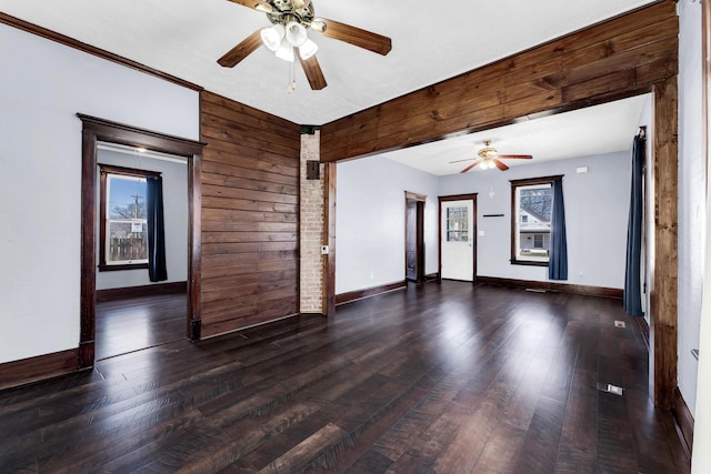 unfurnished room with wooden walls, baseboards, ceiling fan, and wood finished floors