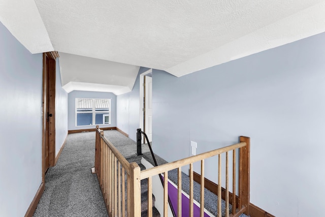 hallway with vaulted ceiling, a textured ceiling, baseboards, and carpet floors