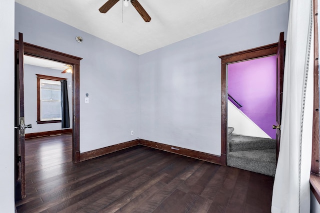 unfurnished room featuring stairs, baseboards, dark wood-type flooring, and a ceiling fan