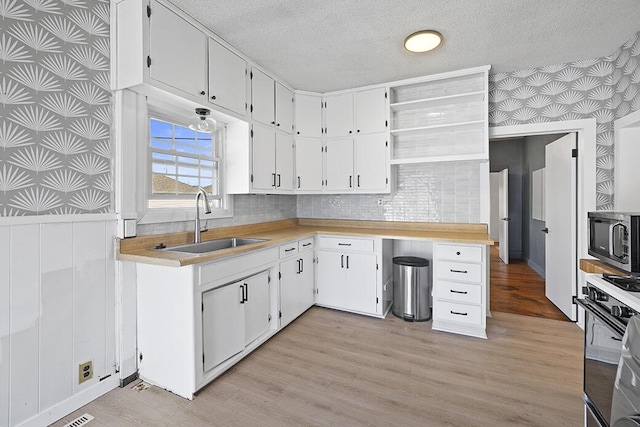 kitchen featuring wallpapered walls, wainscoting, a sink, a textured ceiling, and stainless steel microwave