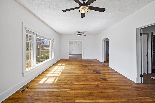 spare room with visible vents, a ceiling fan, a textured ceiling, wood finished floors, and arched walkways