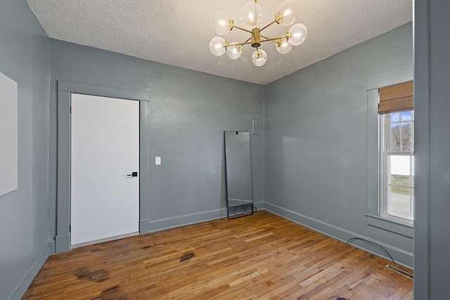 empty room featuring visible vents, hardwood / wood-style flooring, a textured ceiling, baseboards, and a chandelier