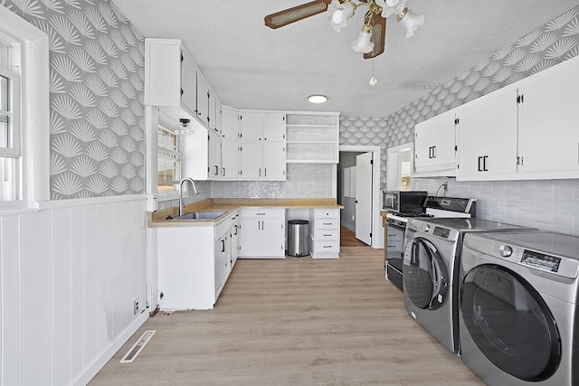 kitchen featuring stainless steel microwave, washer and dryer, wallpapered walls, and a sink