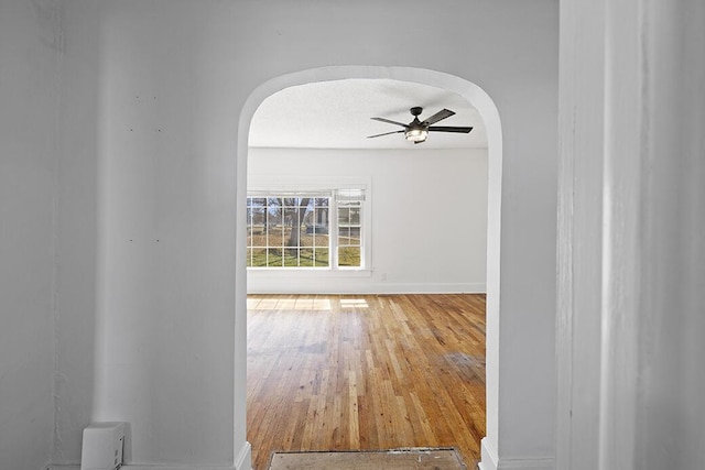 hall with baseboards, arched walkways, a textured ceiling, and wood finished floors