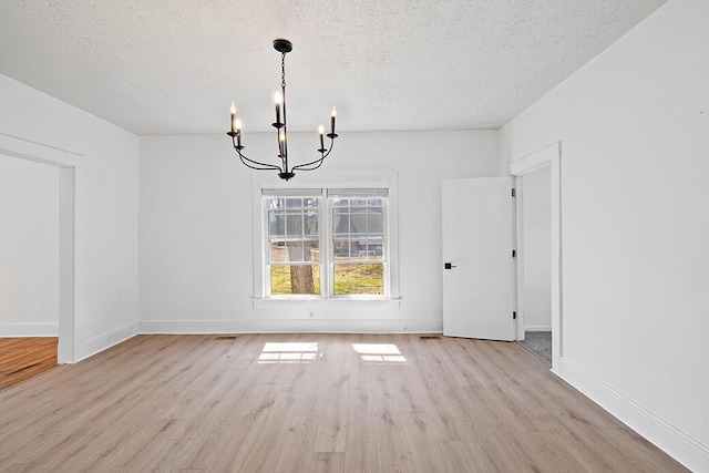 unfurnished dining area with a textured ceiling, wood finished floors, baseboards, and a chandelier