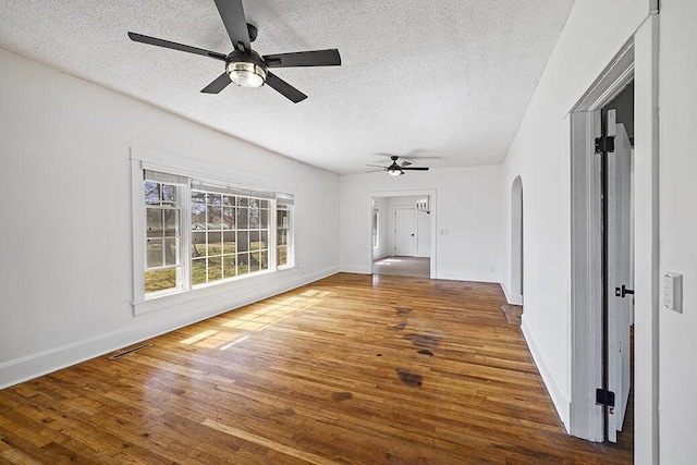 spare room featuring hardwood / wood-style floors, a ceiling fan, visible vents, and arched walkways