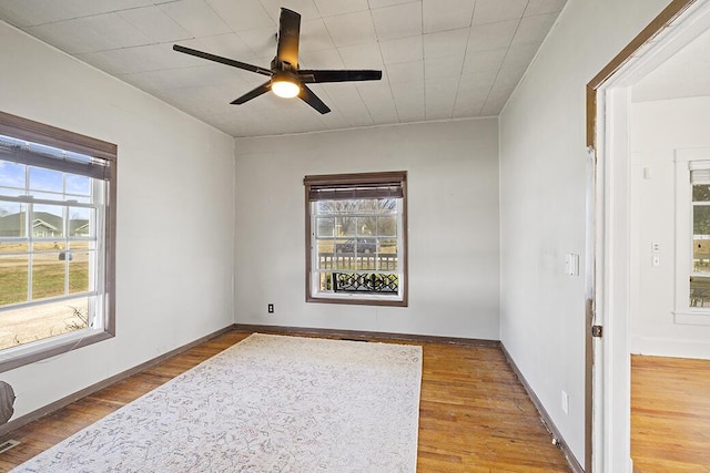 unfurnished room with a ceiling fan, wood finished floors, baseboards, and a wealth of natural light