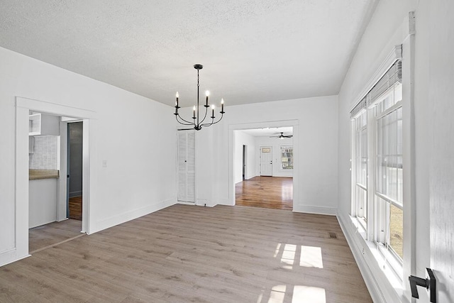 unfurnished dining area featuring baseboards, a textured ceiling, wood finished floors, and ceiling fan with notable chandelier