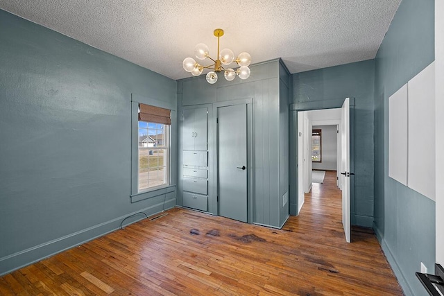 unfurnished bedroom featuring baseboards, a closet, a notable chandelier, a textured ceiling, and wood-type flooring