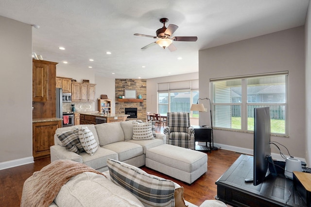 living area featuring a ceiling fan, recessed lighting, a stone fireplace, baseboards, and dark wood-style flooring