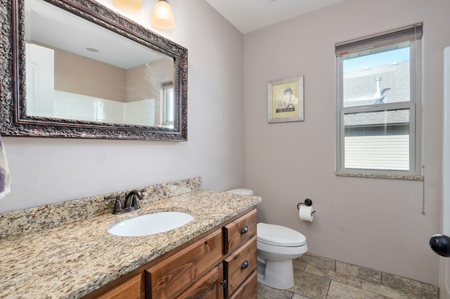 bathroom featuring vanity, toilet, a healthy amount of sunlight, and stone tile flooring