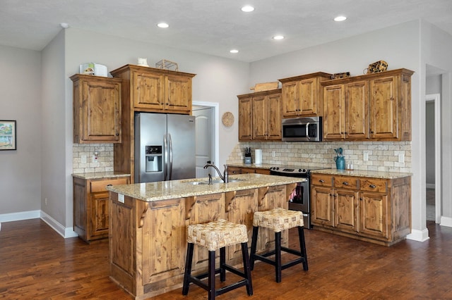 kitchen with brown cabinetry, stainless steel appliances, and a kitchen island with sink