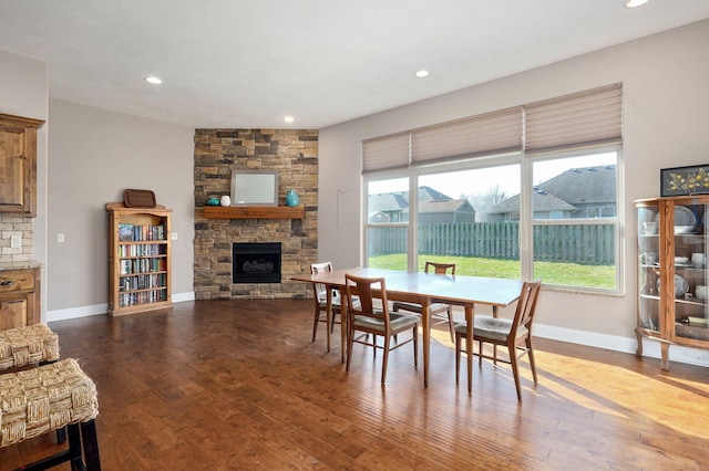 dining room with a stone fireplace, plenty of natural light, baseboards, and dark wood-style flooring