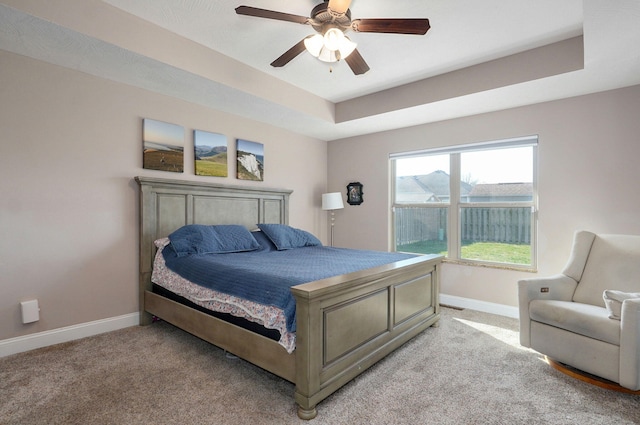 bedroom featuring a raised ceiling, a ceiling fan, baseboards, and light carpet