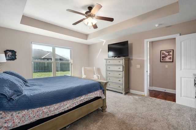 bedroom featuring a raised ceiling, carpet flooring, baseboards, and ceiling fan