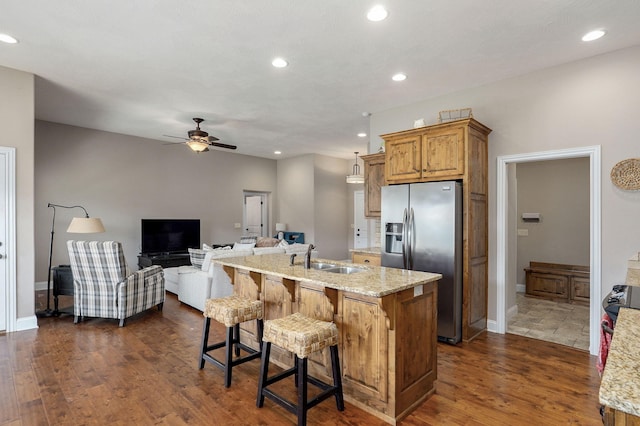 kitchen with light stone counters, dark wood finished floors, ceiling fan, a sink, and stainless steel refrigerator with ice dispenser