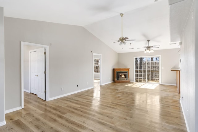 unfurnished living room featuring baseboards, ceiling fan, lofted ceiling, a warm lit fireplace, and light wood-style floors