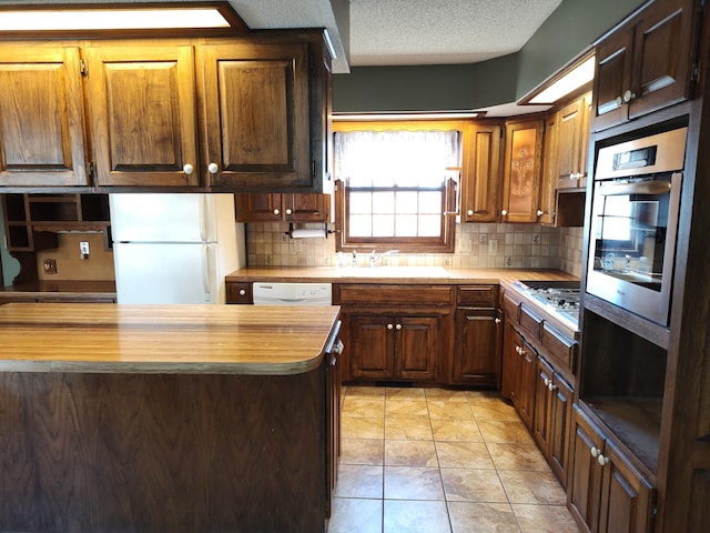 kitchen with wooden counters, decorative backsplash, a textured ceiling, stainless steel appliances, and a sink