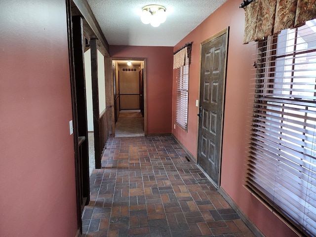 hall featuring baseboards, visible vents, a textured ceiling, and brick floor