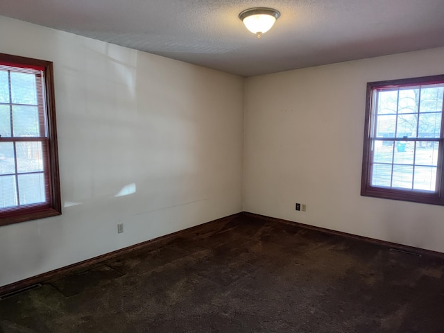 spare room with dark colored carpet, baseboards, and a textured ceiling