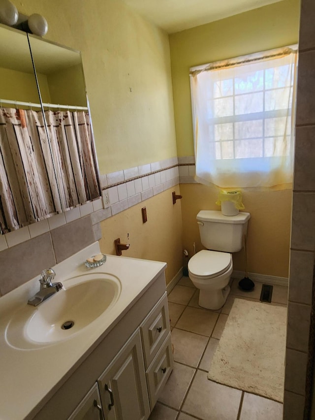 bathroom featuring tile patterned flooring, a wainscoted wall, toilet, vanity, and tile walls