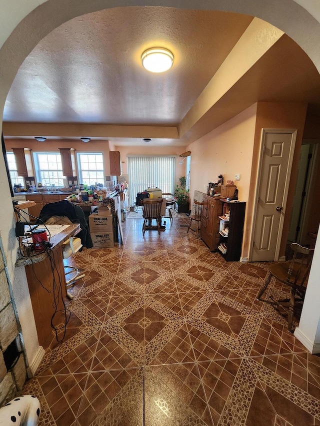 interior space featuring baseboards, arched walkways, a textured ceiling, and tile patterned flooring