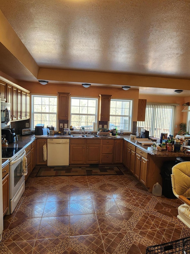 kitchen with a sink, white appliances, a healthy amount of sunlight, and a peninsula