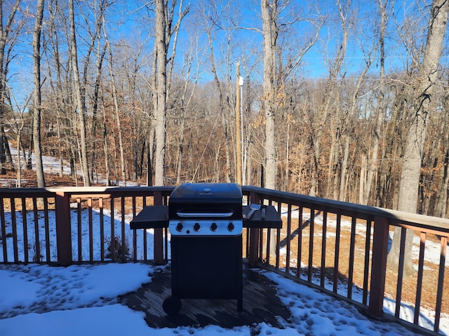 snow covered deck featuring area for grilling and a forest view