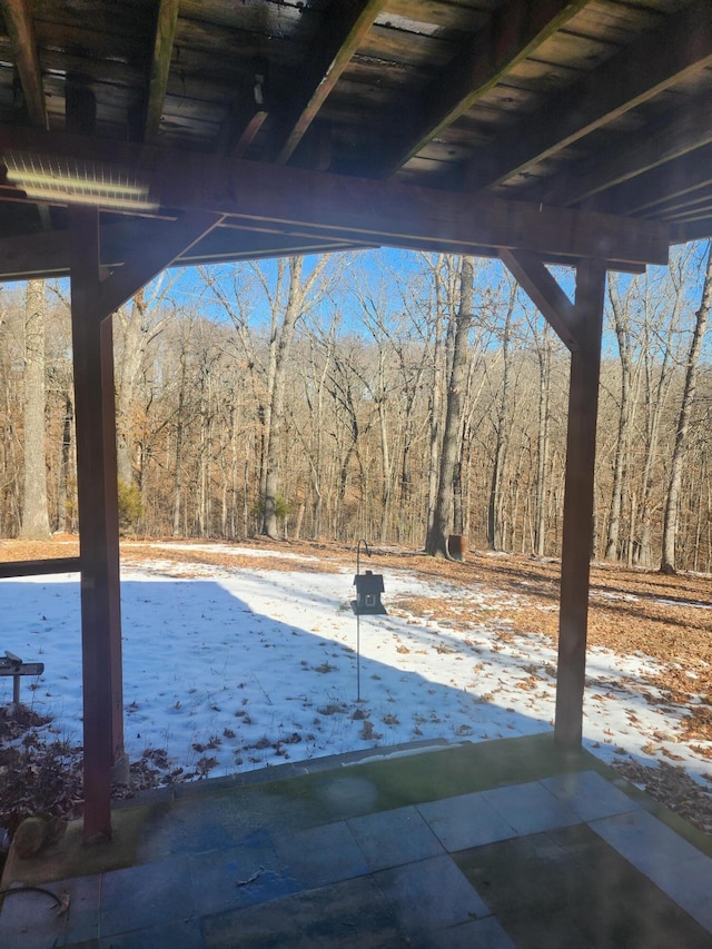 snow covered patio with a forest view