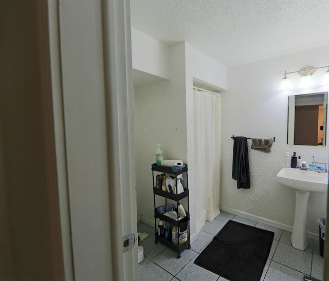 full bath featuring a shower with curtain, baseboards, a sink, a textured ceiling, and tile patterned floors