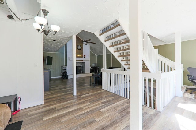 interior space with wood finished floors, baseboards, a fireplace, vaulted ceiling, and ceiling fan with notable chandelier