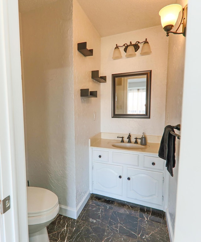 bathroom with baseboards, toilet, a textured wall, marble finish floor, and vanity