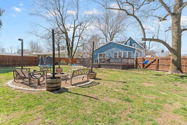 view of yard featuring a gate, a fenced backyard, a fire pit, a deck, and a trampoline