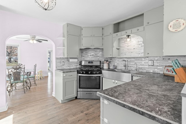 kitchen with dark countertops, ceiling fan, stainless steel range with gas stovetop, light wood-type flooring, and a sink