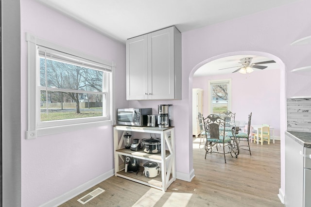 kitchen with arched walkways, visible vents, stainless steel microwave, and light wood-type flooring