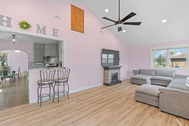 living room with a ceiling fan, visible vents, light wood finished floors, a fireplace, and arched walkways