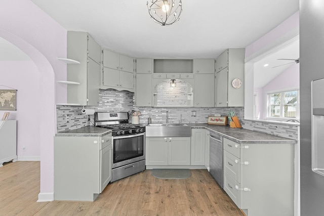 kitchen featuring tasteful backsplash, open shelves, light wood-style flooring, appliances with stainless steel finishes, and a sink