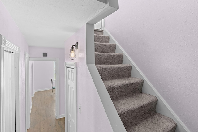 staircase with wood finished floors and a textured wall