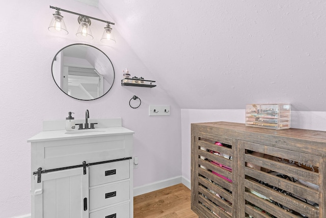 bathroom featuring baseboards, wood finished floors, vanity, and vaulted ceiling