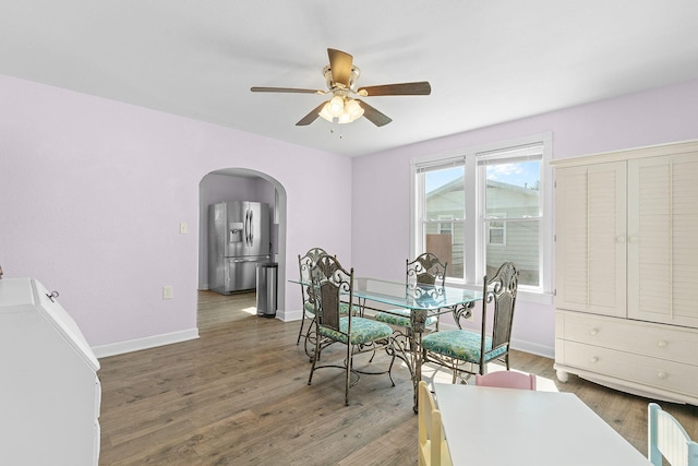 dining area with baseboards, wood finished floors, arched walkways, and ceiling fan