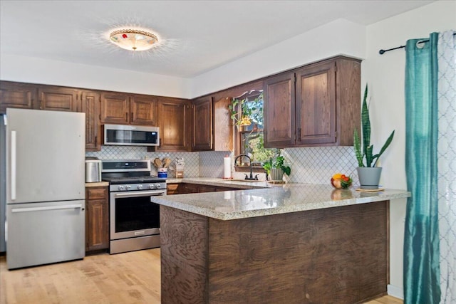 kitchen with a sink, tasteful backsplash, appliances with stainless steel finishes, a peninsula, and light wood finished floors