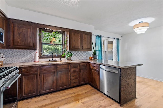 kitchen with dark brown cabinetry, light stone counters, light wood-style floors, stainless steel appliances, and a sink