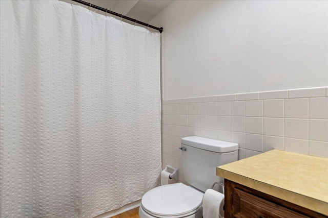 bathroom with a shower with shower curtain, toilet, tile walls, and wainscoting