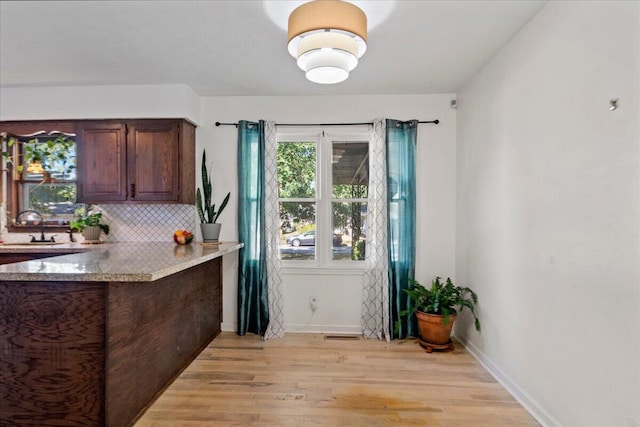 kitchen featuring a peninsula, light wood-style flooring, tasteful backsplash, and a sink