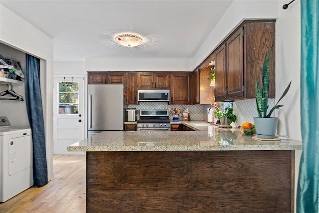 kitchen with a peninsula, washer / clothes dryer, a sink, decorative backsplash, and stainless steel appliances