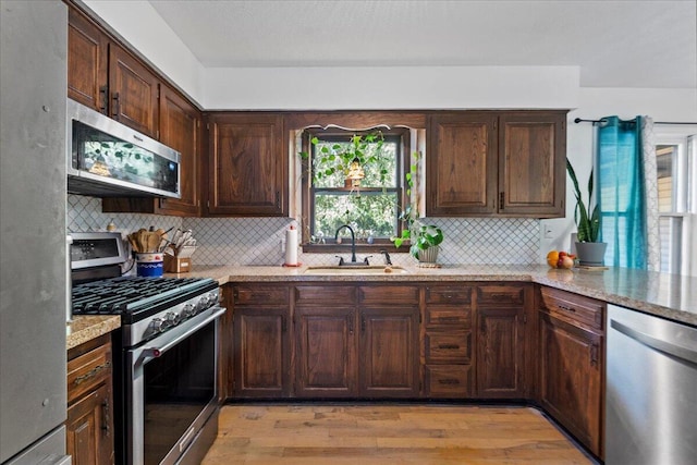 kitchen with a sink, stainless steel appliances, dark brown cabinets, and light wood-style flooring